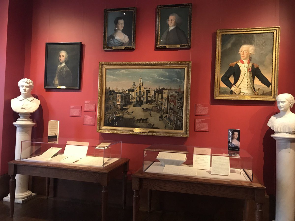 Two exhibit cases with wall paintings hanging above and a marble bust on either side